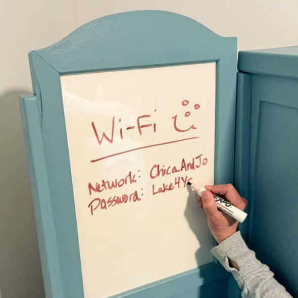 guest room essentials in a thrifted cabinet for amenities - wifi information on a dry erase board